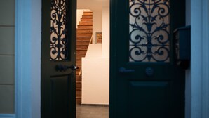 A hallway with a wooden staircase, a green door with decorative metalwork, and a white wall with a framed picture. - Appartementhaus Hohe Tauern (Obervellach)