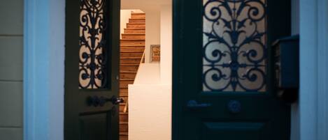 A hallway with a wooden staircase, a green door with decorative metalwork, and a white wall with a framed picture.
