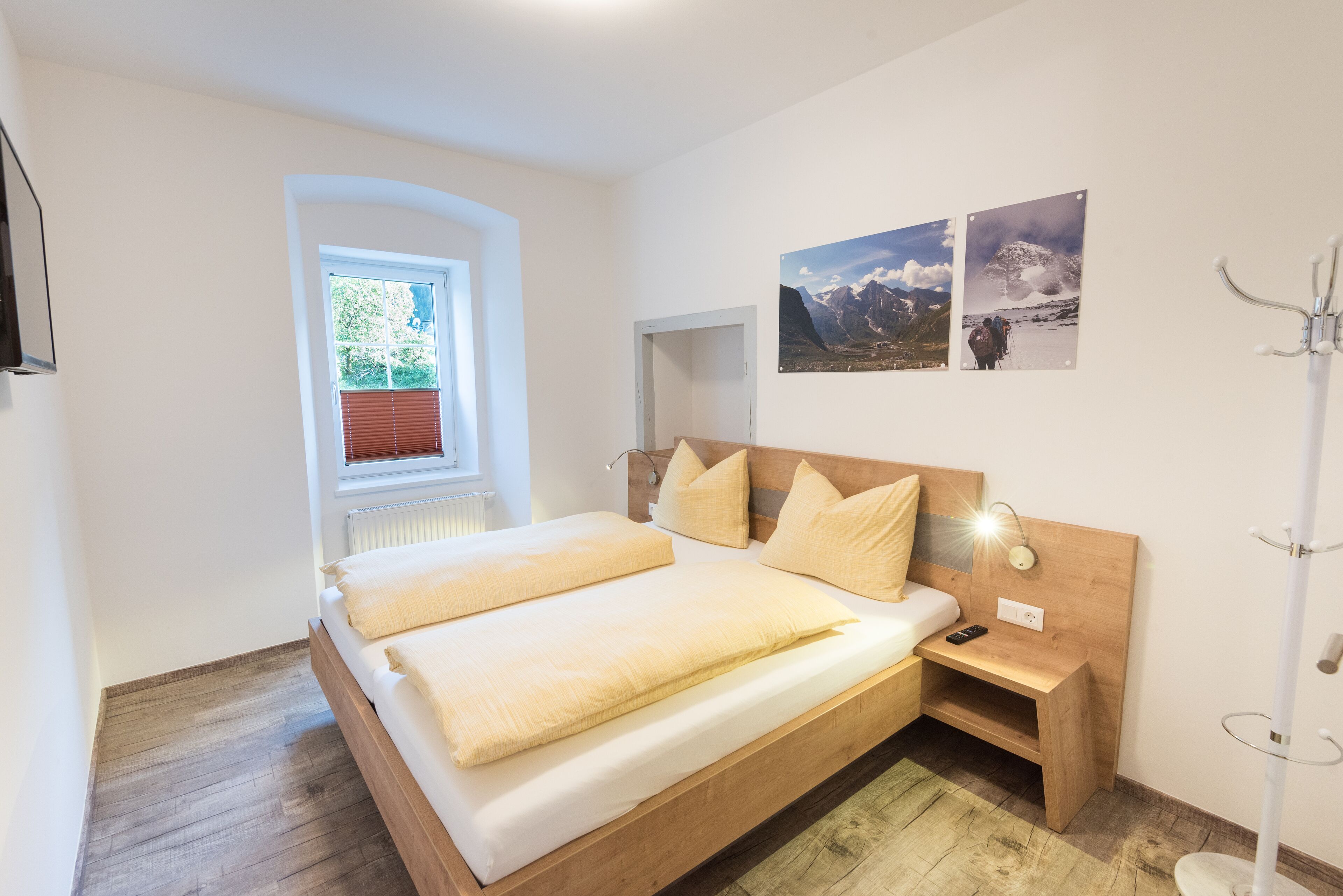 A bedroom with a wooden bed, a bedside table with a lamp, and two framed pictures on the wall.