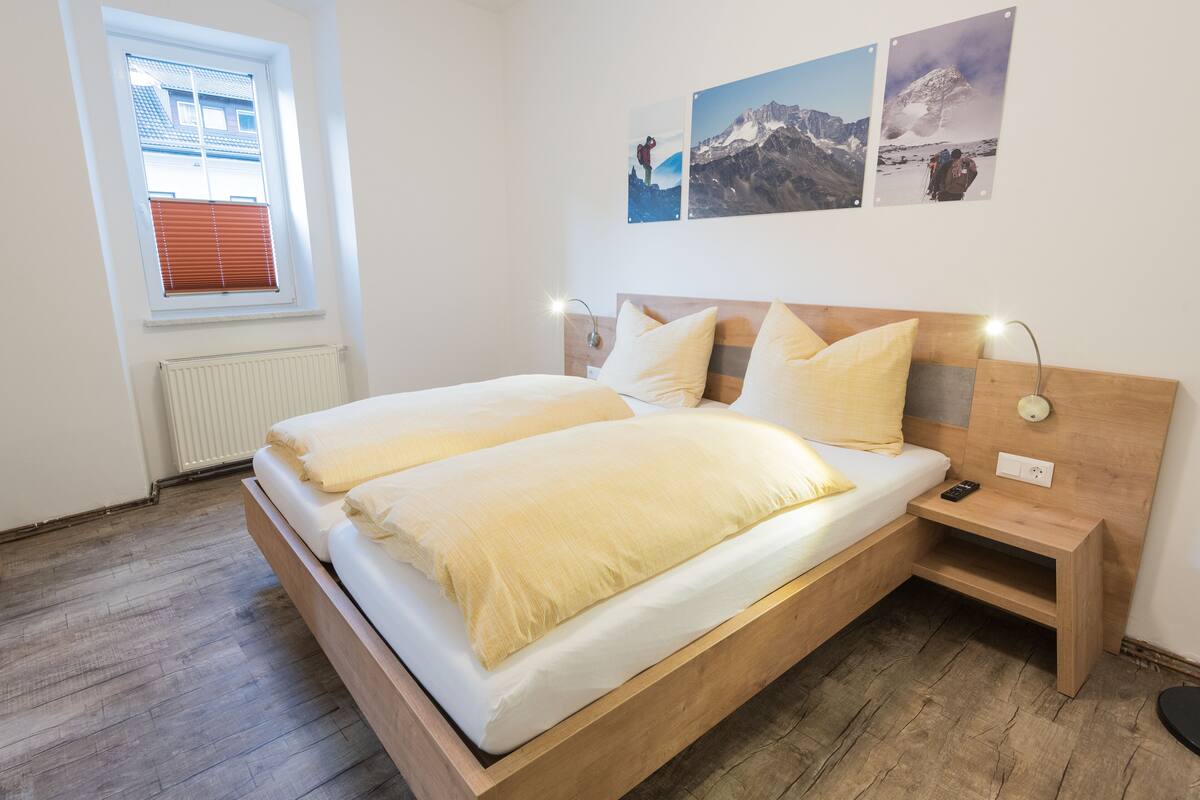 Um quarto moderno com cama de madeira, abajures e arte na parede com tema de montanhas.