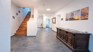 A hallway with a wooden staircase, a dark tiled floor, a wooden cabinet, and framed artwork on the walls. - Appartementhaus Hohe Tauern (Obervellach)