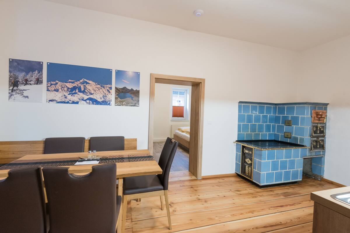 Uma sala de jantar com mesa e cadeiras de madeira, uma cozinha com azulejos azuis e vista para a montanha.