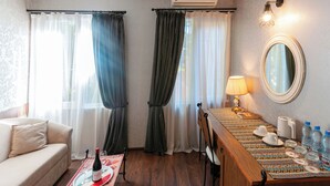 A hotel room with a sofa, a dining table with a placemat, a mirror, and a wall-mounted air conditioner. - Wine Story Hotel  (Tbilisi)