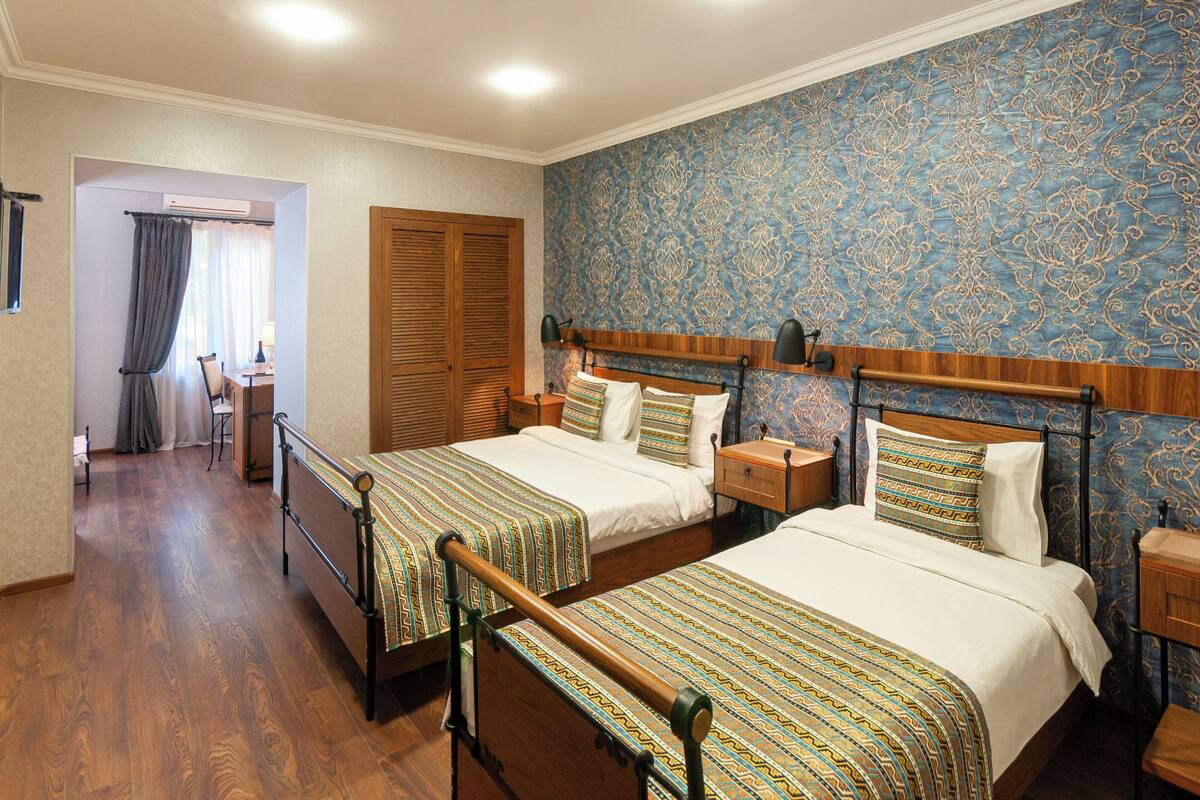 A hotel room with two beds, wooden headboards, a nightstand, a desk, and a chair.