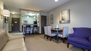 A hotel room with a sofa, a purple armchair, a dining area with a table and chairs, a kitchen area, and a patterned carpet. - Vrbo Property (Wisconsin Dells)