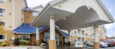 A hotel with a covered entrance, multiple floors, and a parking lot.