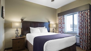 A hotel room with a large bed, two bedside tables, a nightstand, a window with patterned curtains, and a view of the outside. - Vrbo Property (Wisconsin Dells)