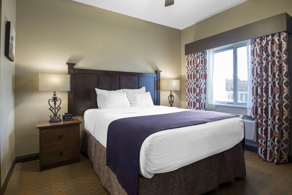 A hotel room with a large bed, two bedside tables, a nightstand, a window with patterned curtains, and a view of the outside. - Vrbo Property (Wisconsin Dells)