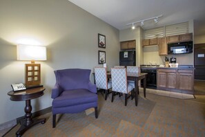 A compact hotel room with a purple armchair, a small table with a lamp, a kitchenette with a microwave and refrigerator, and a patterned carpet. - Vrbo Property (Wisconsin Dells)