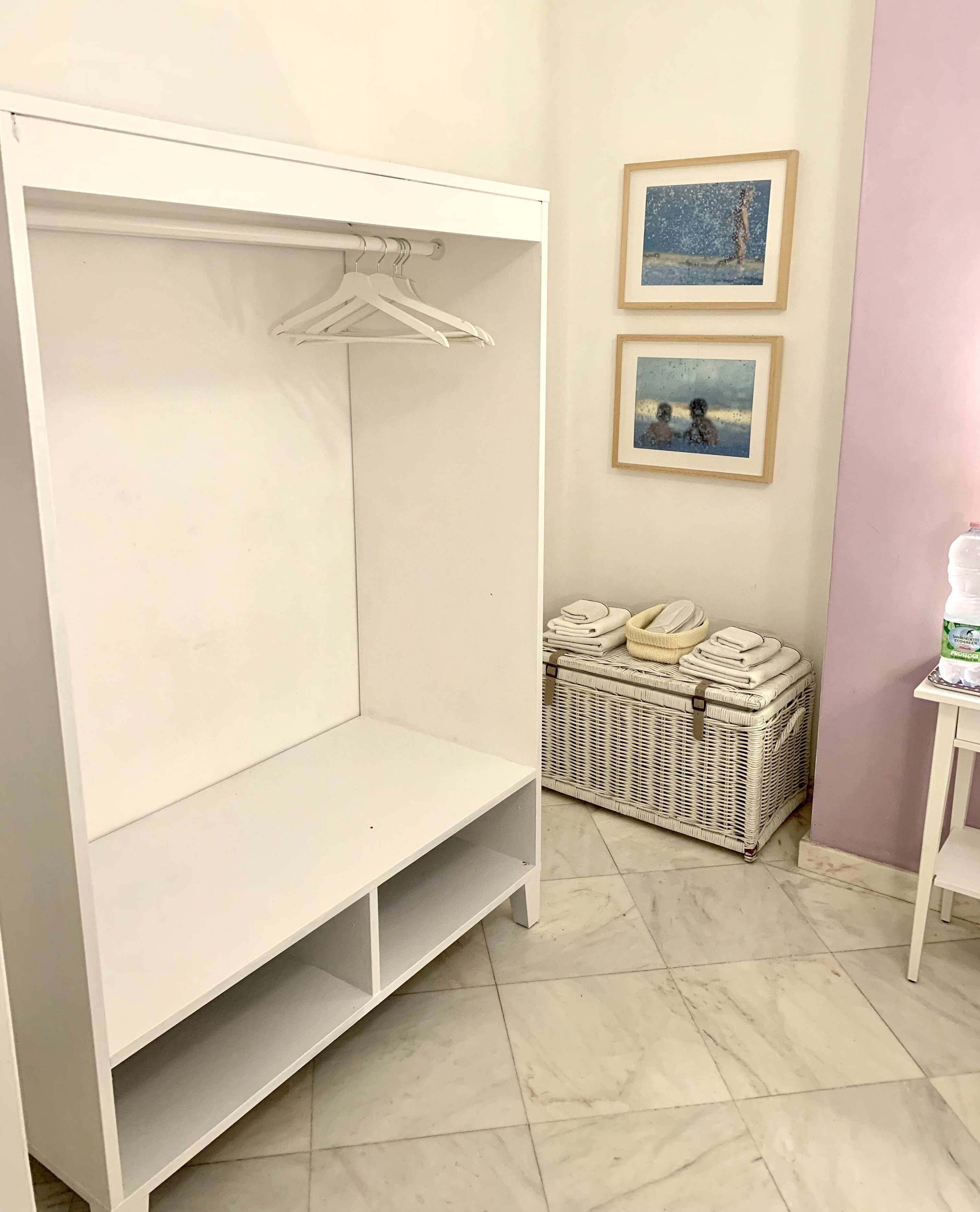 A white wardrobe with a hanging rod and a folded blanket on the floor.