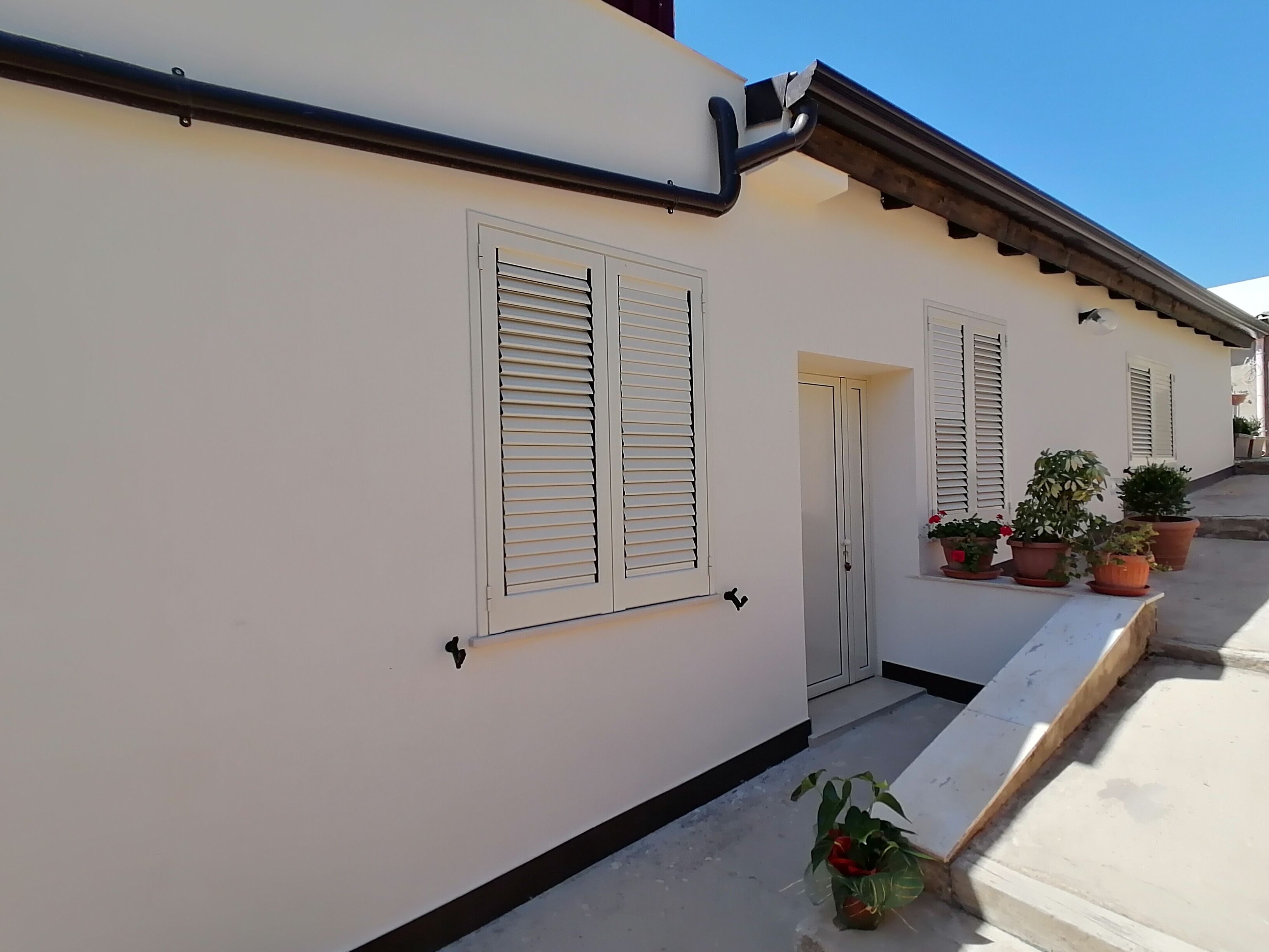 A white building with shutters, a door, and potted plants.