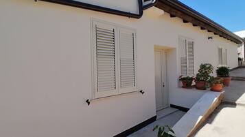 A white building with shutters, a door, and potted plants.