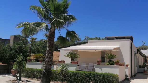 A modern building with a flat roof, a covered patio area with outdoor seating, and various potted plants. - Vacation Home Villa Tropia (Camastra)