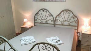 A neatly made bed with a headboard, two bedside tables with lamps, and two folded towels on the bed. - Vacation Home Villa Tropia (Camastra)