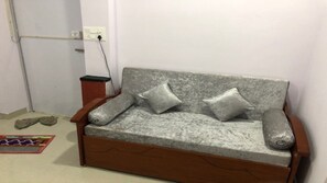A grey sofa with wooden armrests and two pillows, positioned against a white wall with a power outlet.