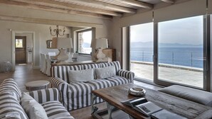 Un amplio salón con un ventanal grande con vista al mar, techo de madera y muebles a rayas.