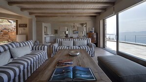 Un salón amplio con sofás a rayas, una mesa de centro de madera con un libro, y un ventanal con vistas al mar.