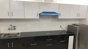 Eine moderne Küche mit weißen Schränken, einer schwarzen Arbeitsplatte, einem Edelstahlkühlschrank und einer blauen Dunstabzugshaube.