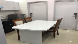 Eine kleine Küche mit einem weißen Tisch, Holzstühlen und einem schwarzen Gerät.