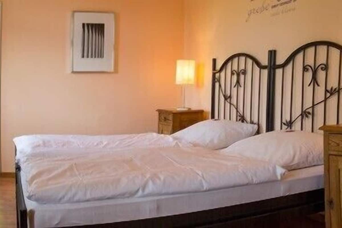 A bedroom with a bed, a bedside table, a lamp, and a window.
