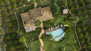 Vue aérienne d’une propriété dotée d’une piscine, d’un espace patio et d’un jardin avec différents arbres.