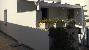 Ein modernes, zweistöckiges Gebäude mit flachem Dach und weißen Außenwänden. Am Erdgeschoss befinden sich Blumentöpfe mit gelben Blüten.