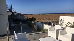 Eine Dachterrasse mit weißen Korbmöbeln, einem Glasgeländer und Blick auf das Meer.