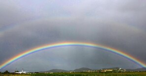 Un arcobaleno che si inarca sopra un paesaggio con montagne ed edifici sullo sfondo.