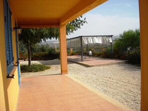 Ein überdachter Patio-Bereich mit Sitzgelegenheiten im Freien und Blick auf ein Gebäude im Hintergrund.