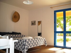 Ein Schlafzimmer mit Bett, Stuhl, Spiegel und einer Tür, die zu einem Außenbereich führt.