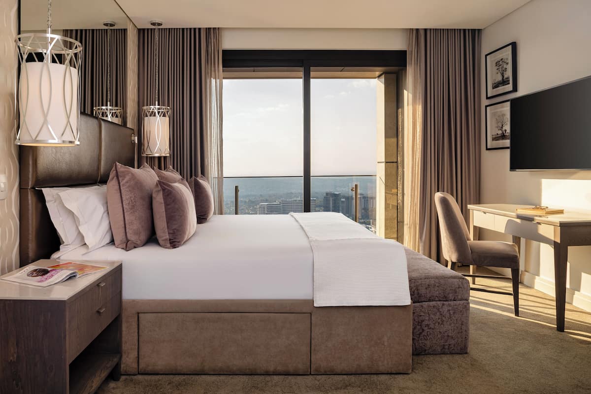 A modern hotel room with a large bed, a desk, and a view of the city.