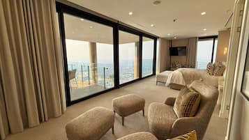 Quarto de hotel espaçoso com uma varanda grande, uma cama, duas poltronas e uma televisão.