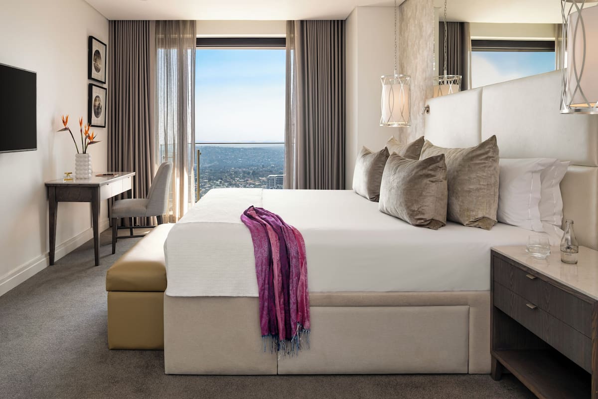 A modern hotel room with a large bed, a desk, and a view of the city.