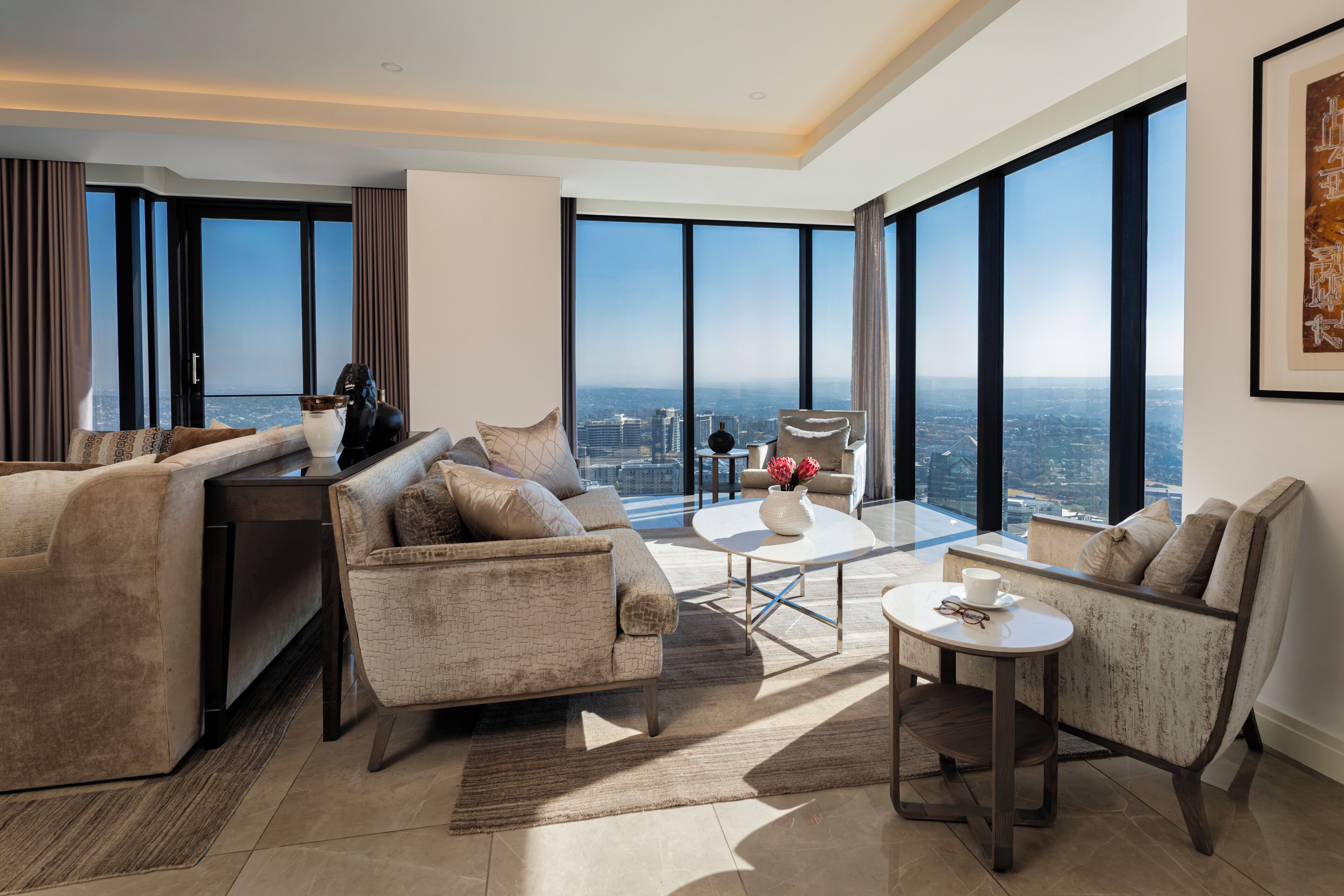 Una sala de estar moderna con un sofá, sillones y una mesa de centro. Amplios ventanales ofrecen vistas a la ciudad.