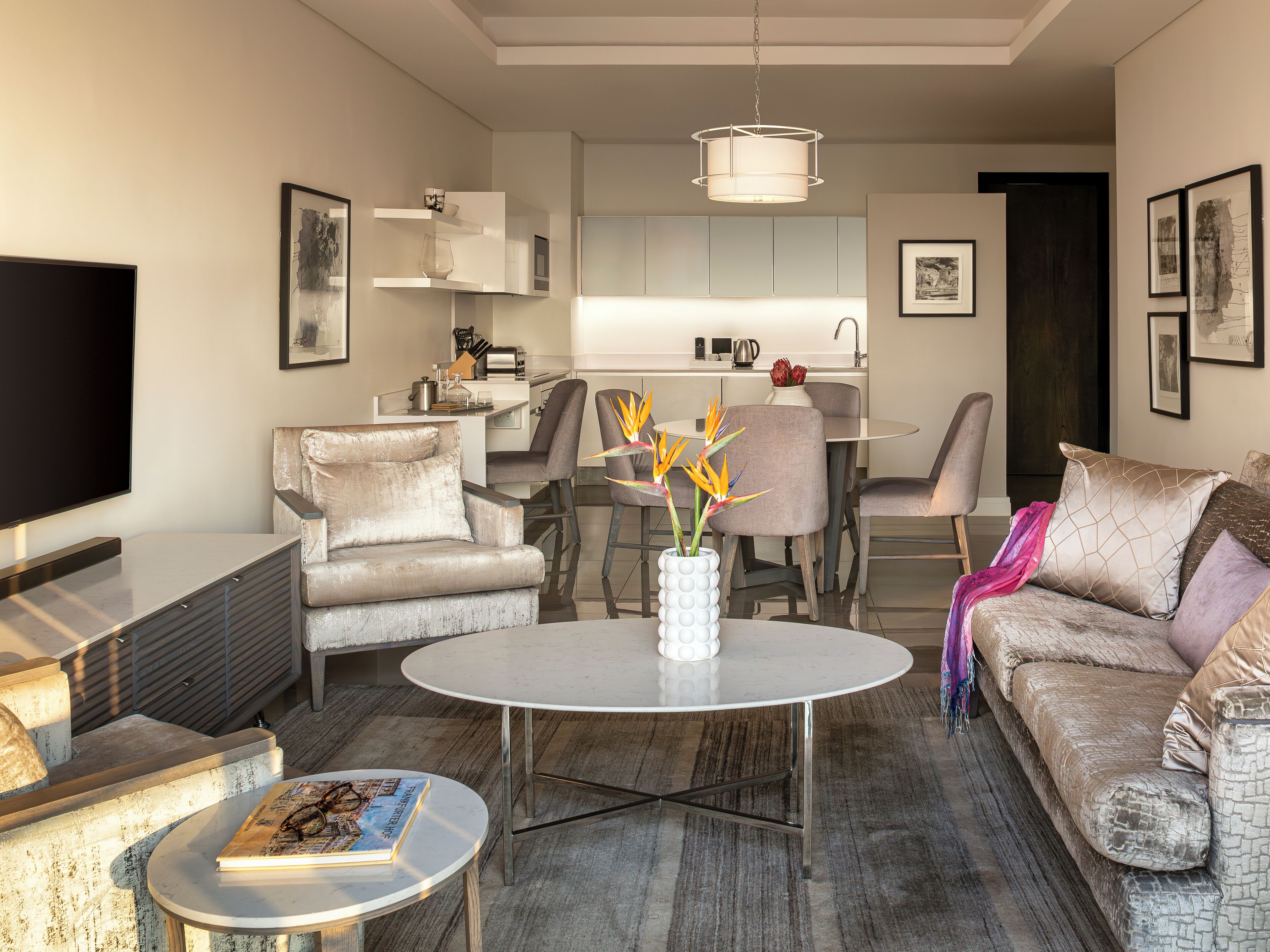 A modern living room with a flat-screen TV, a sofa, a coffee table, and a dining area with chairs and a table.
