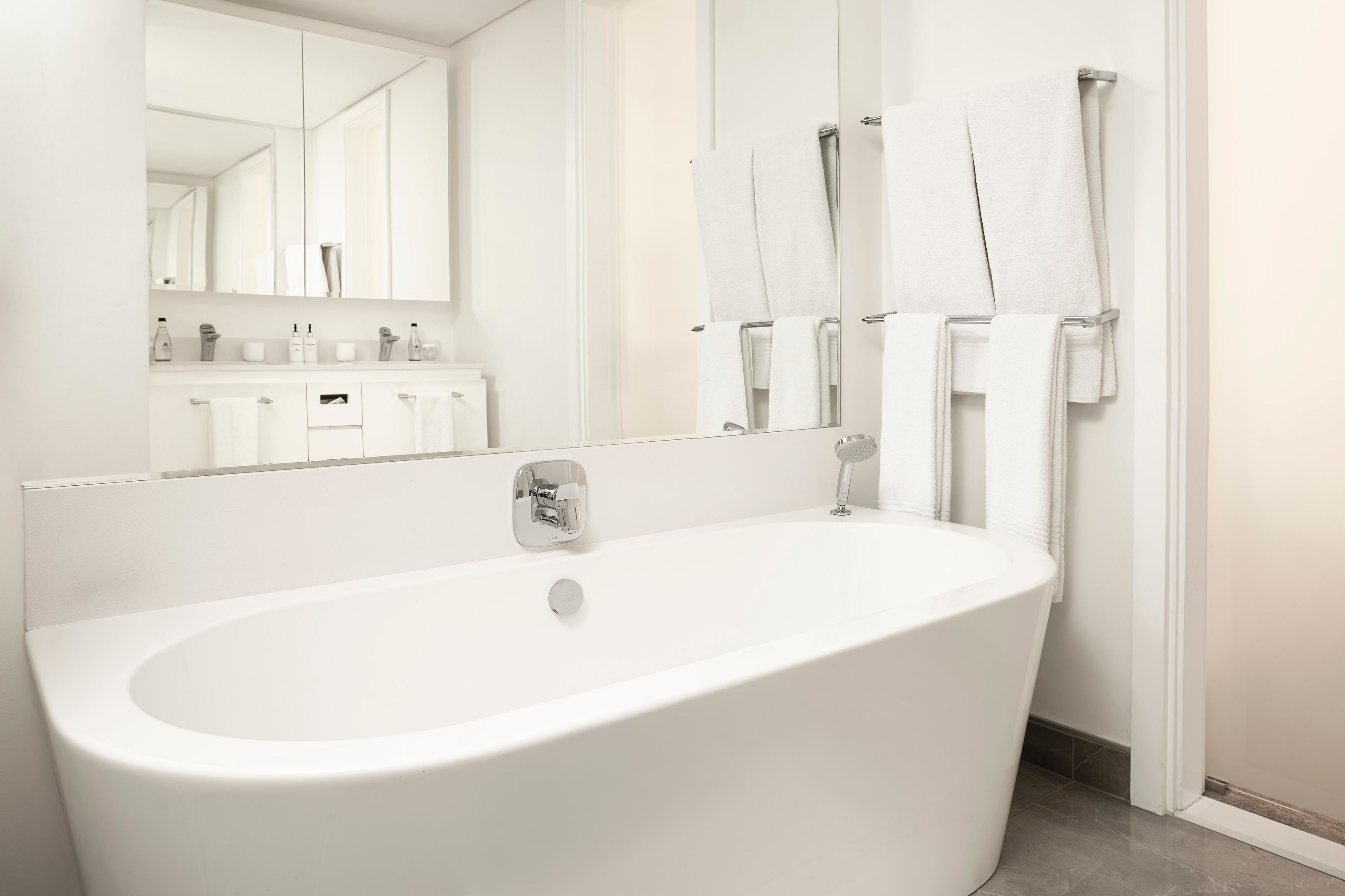 Ein modernes Badezimmer mit einer freistehenden Badewanne, einem großen Spiegel und einem Handtuchhalter mit mehreren Handtüchern.