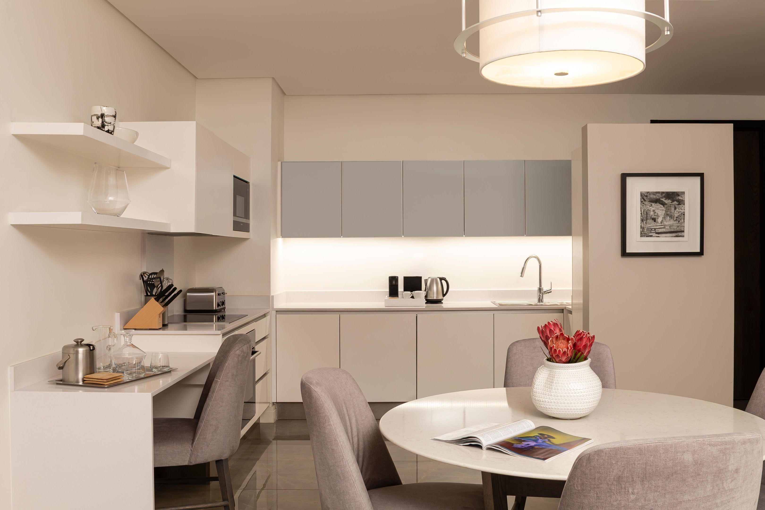 Une cuisine moderne avec des meubles blancs, une table à manger avec des chaises et un luminaire suspendu.
