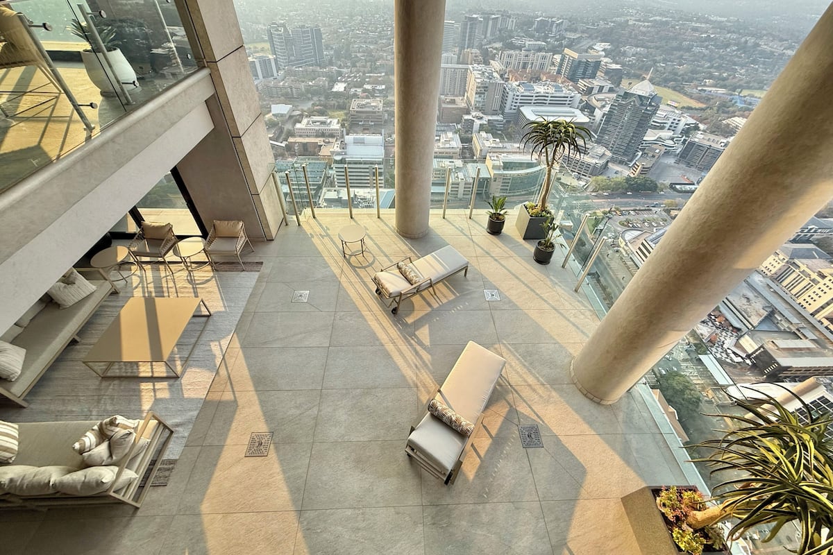 A high-rise building with a glass balcony, outdoor seating, and potted plants.