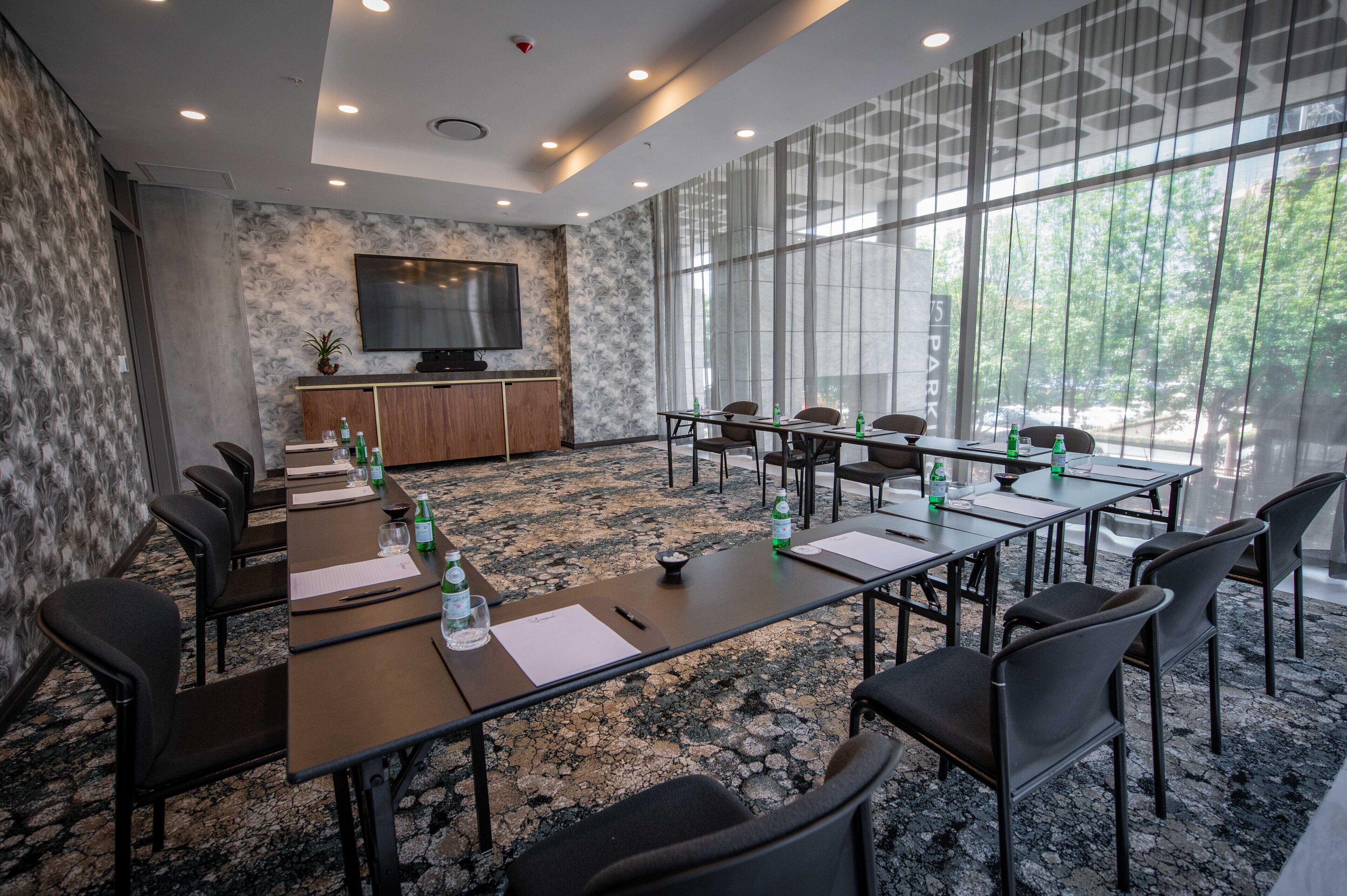 A conference room with a long table, chairs, a TV, and a large window with a view of trees.