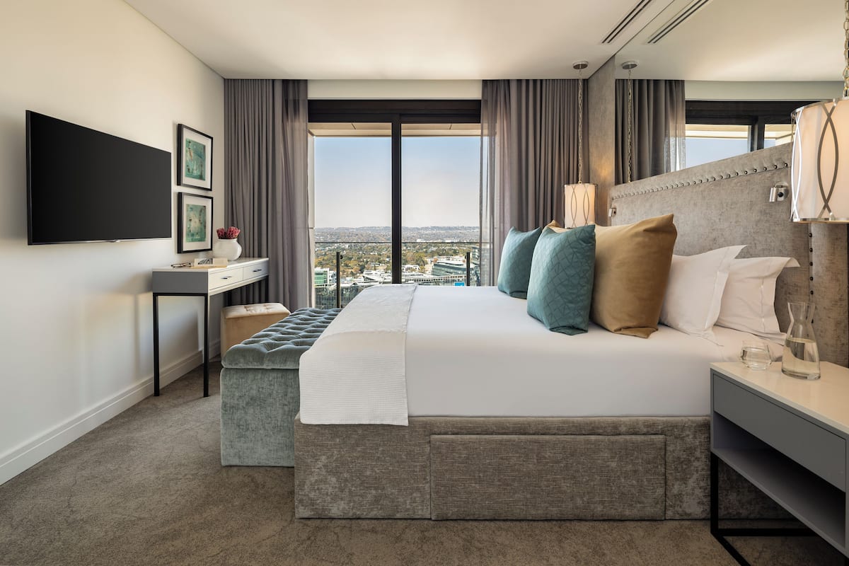 A modern hotel room with a large bed, a flat-screen TV, a desk, and a view of the city.