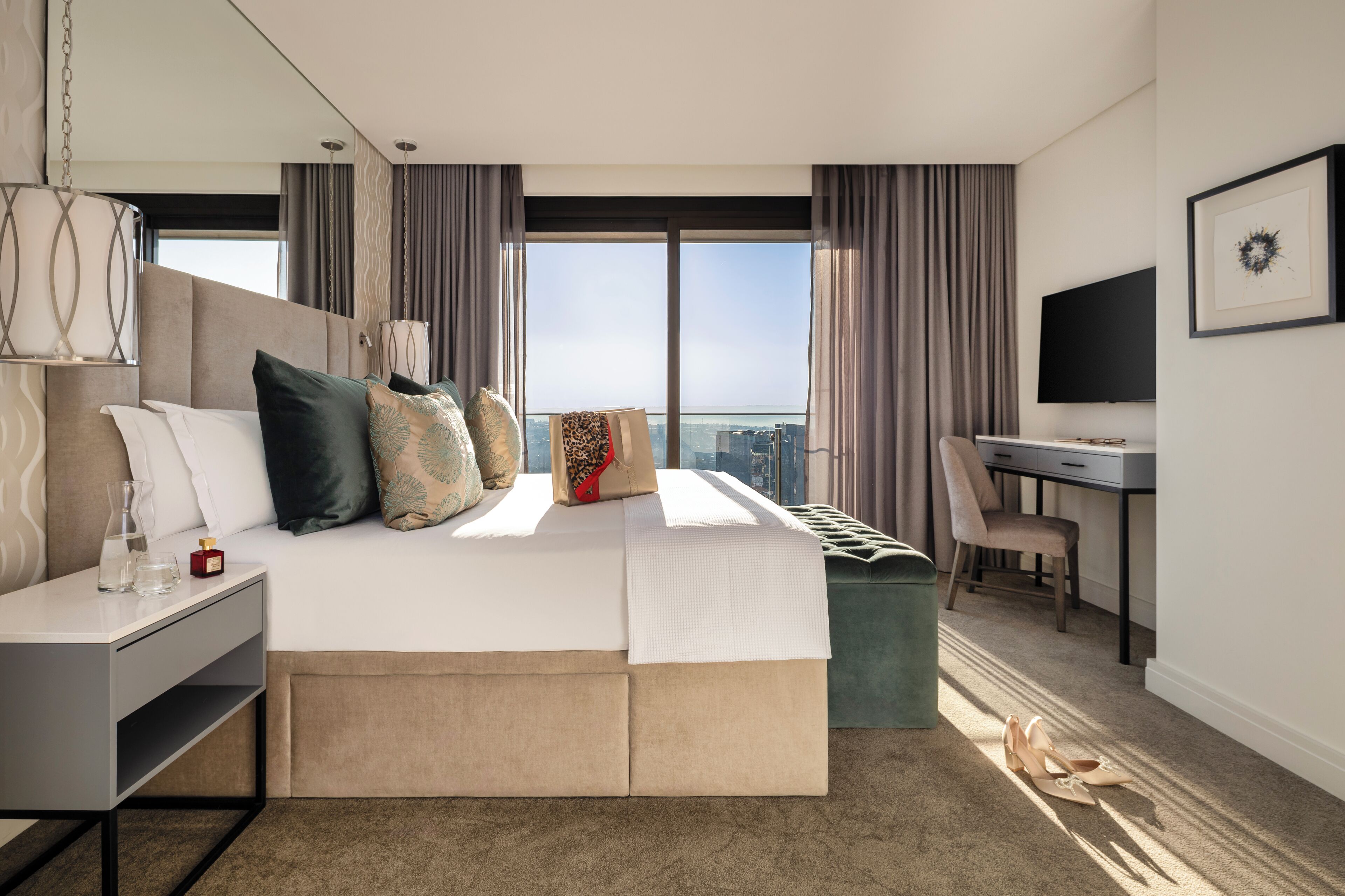 A modern hotel room with a large bed, a desk, and a view of the city.
