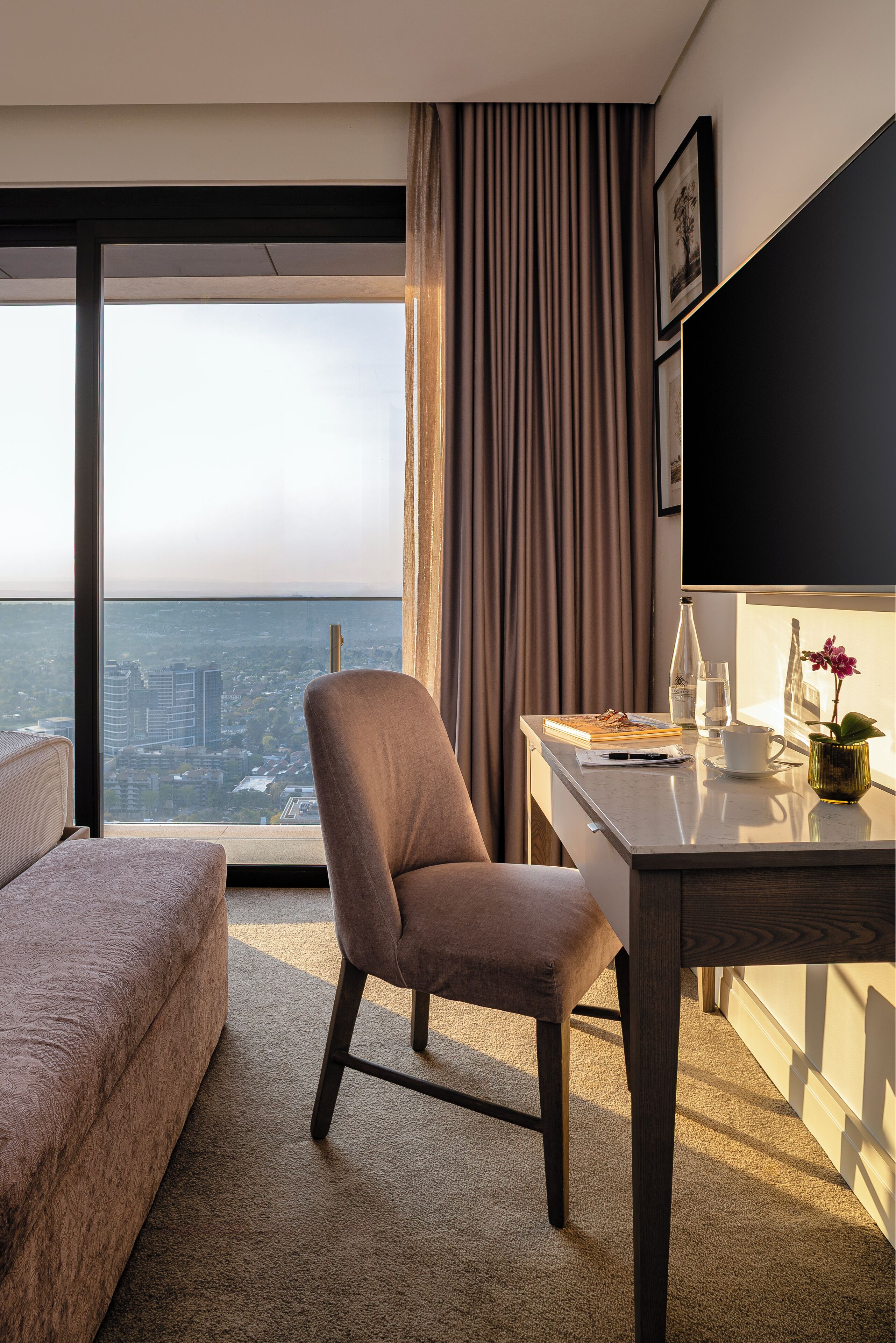 Habitació d'hotel moderna amb un gran finestral, un escriptori amb un ordinador portàtil, una cadira, un sofà i vista a la ciutat.