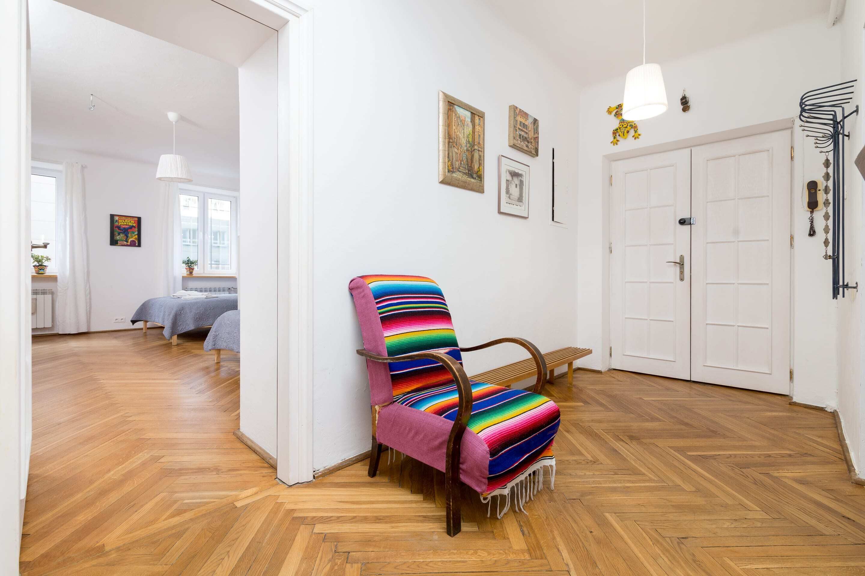 A room with a wooden herringbone floor, a colorful striped armchair, a white door, and a bed with a gray bedspread.