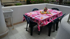 Een balkon met een tafel, bedekt met een kleurrijke tafelkleed, vier stoelen en een kleine decoratieve plant.