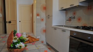 Een keuken met een fornuis, oven en kastjes. Er staat een tafel met een tafelkleed met bloemen en een bloevas.