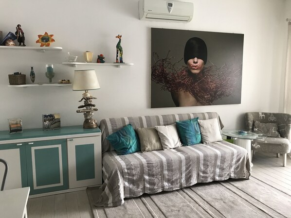 Un salon avec un canapé à rayures, des coussins turquoise, une table basse en verre et un tableau accroché au mur.