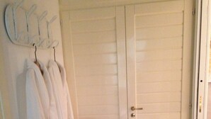 Une salle de bain avec une porte blanche, une chaise et plusieurs peignoirs blancs suspendus à des crochets.