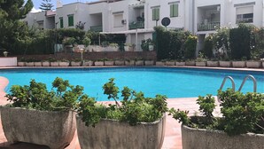 Une piscine entourée de plantes en pot et un bâtiment blanc doté de balcons.
