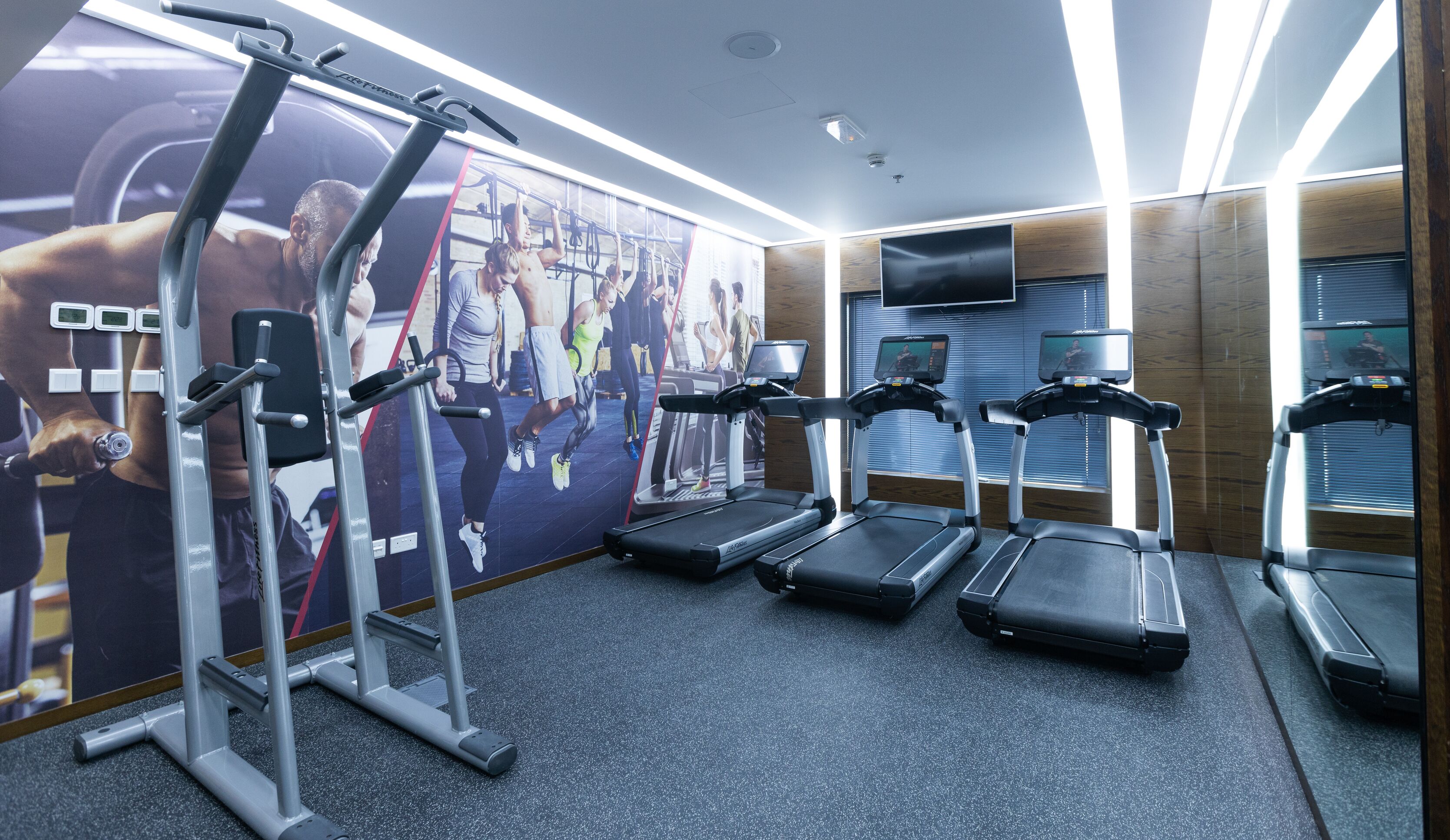 A gym with treadmills, a weight machine, and a large motivational poster on the wall.