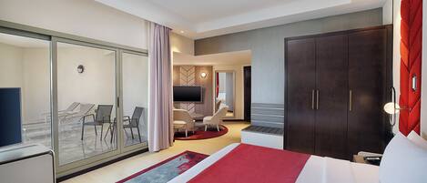 Une chambre d’hôtel dotée d’un grand lit, d’une télévision, d’un bureau et d’un coin salon avec des chaises et une table.